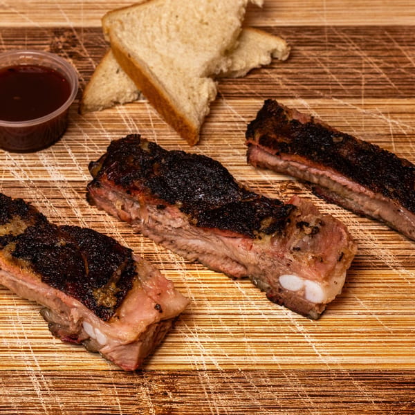 Three Hot Spot Barbecue ribs with dark crust, white bread, and a side of BBQ sauce.