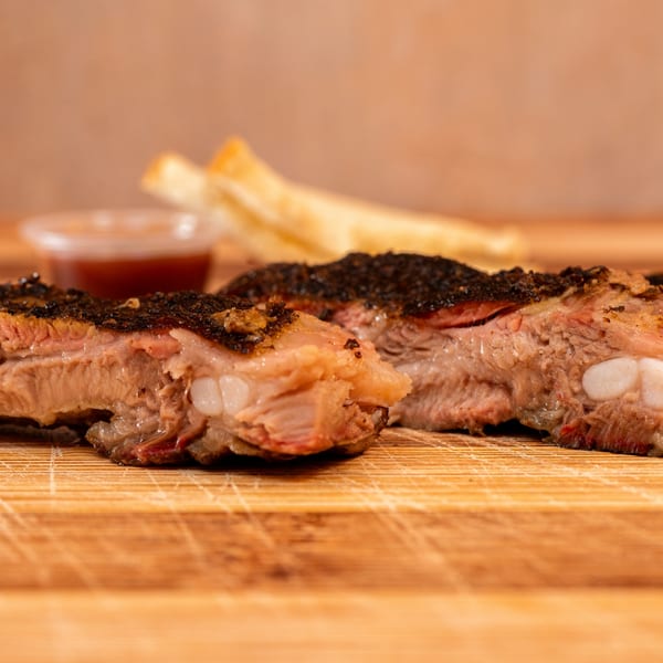 Close-up of Hot Spot Barbecue ribs with a dark crust, served with fries and sauce.