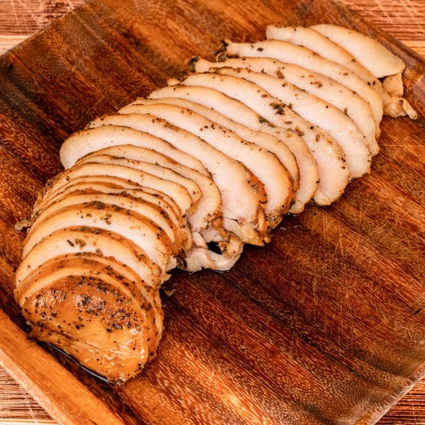 Slices of seasoned, cooked chicken breast arranged on a rustic wooden cutting board.